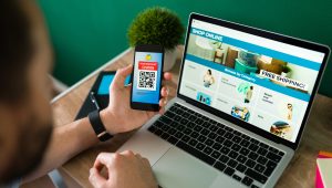 Young man using a discount coupon on his smartphone to do some online shopping on the laptop